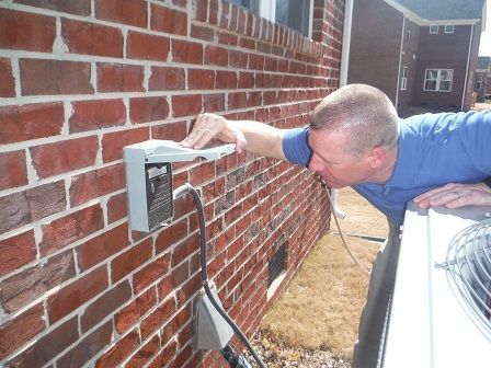 Man inspecting an electrical box on a brick wall next to an AC unit.