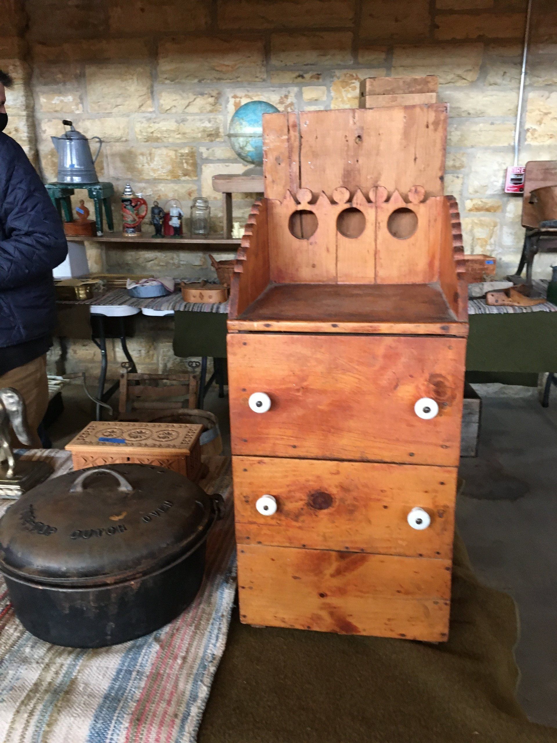 A wooden dresser with white knobs sits next to a black pot.