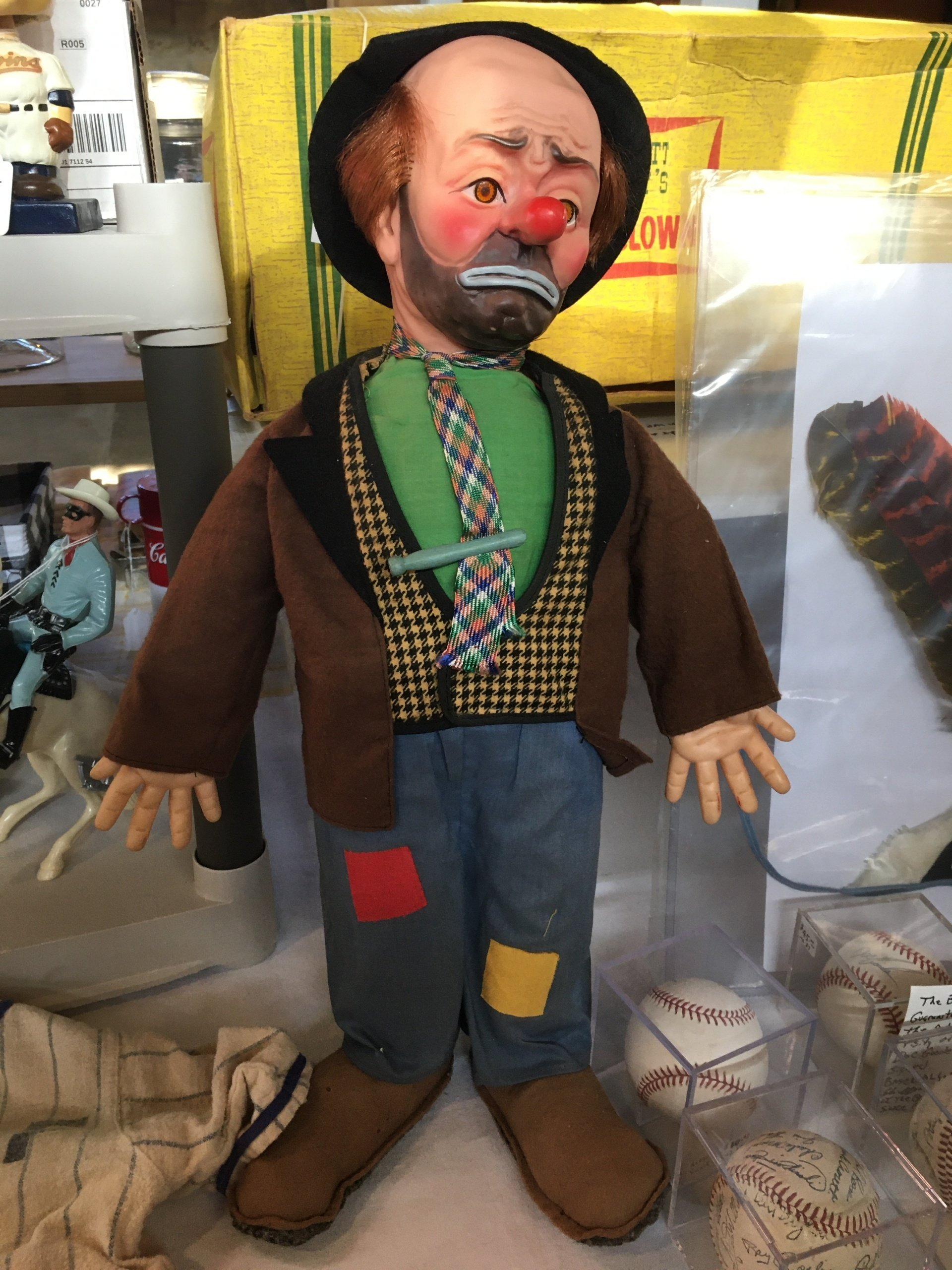 A clown doll is standing in front of some baseballs