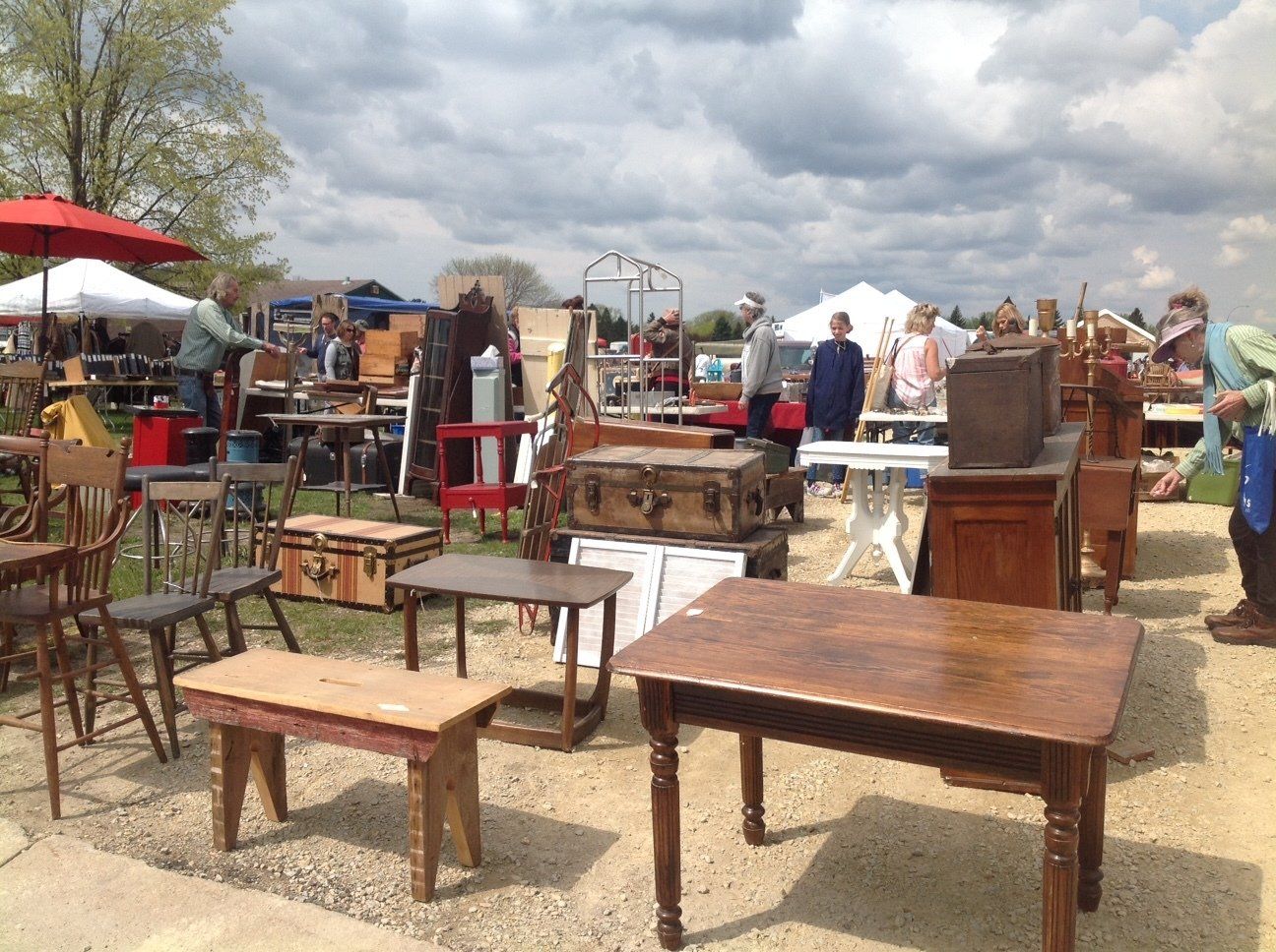 A group of people are standing around tables and chairs at a flea market.