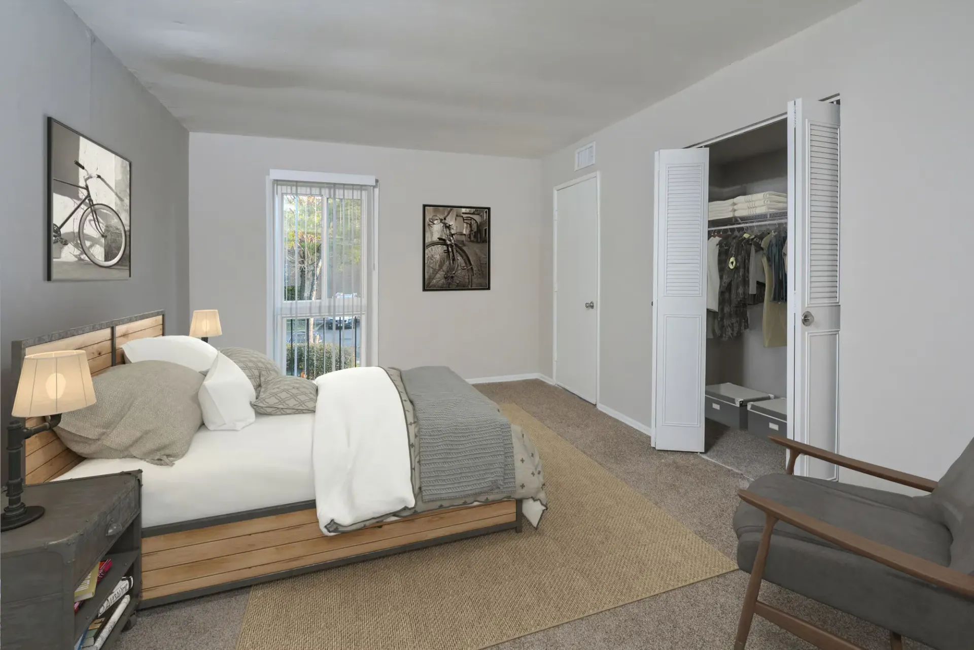 Bedroom in an apartment with a wooden platform bed, two lamps, a window, and an open closet at Metro Pointe in Baltimore, MD.