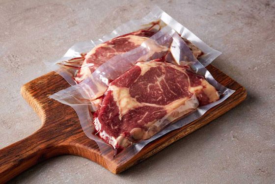 The meat is wrapped in plastic and sitting on a wooden cutting board.