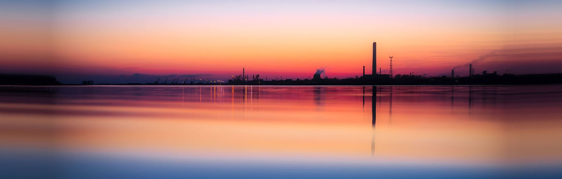 A sunset over a body of water with a factory in the distance.