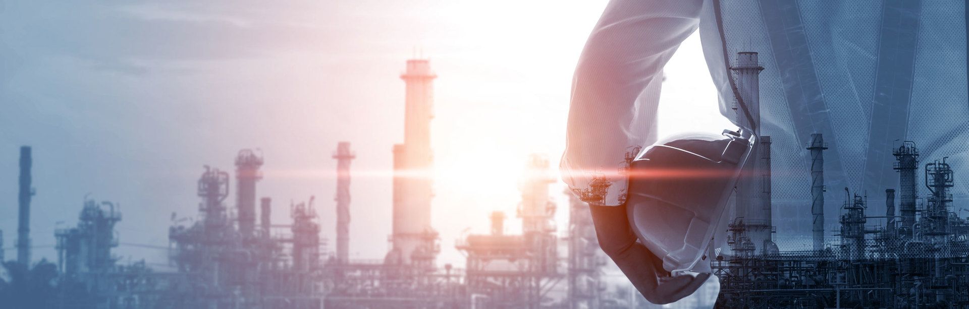 A man is holding a hard hat in front of a factory.