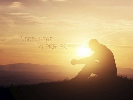 A man is kneeling down in front of a sunset and praying.
