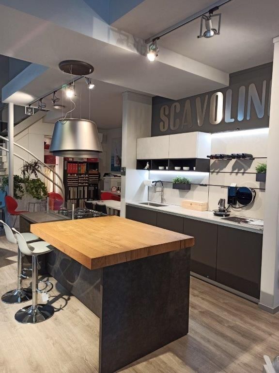 Showroom di cucine moderne con isola, sgabelli da bar, mobili bianchi e grande insegna a parete SCAVOLINI.