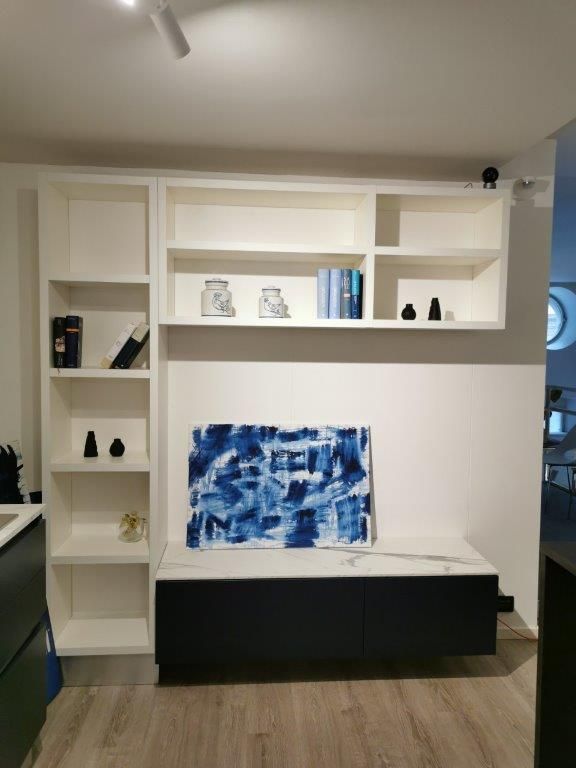 Mobile a parete minimalista bianco con mensole, panca nera e quadro astratto blu in soggiorno.
