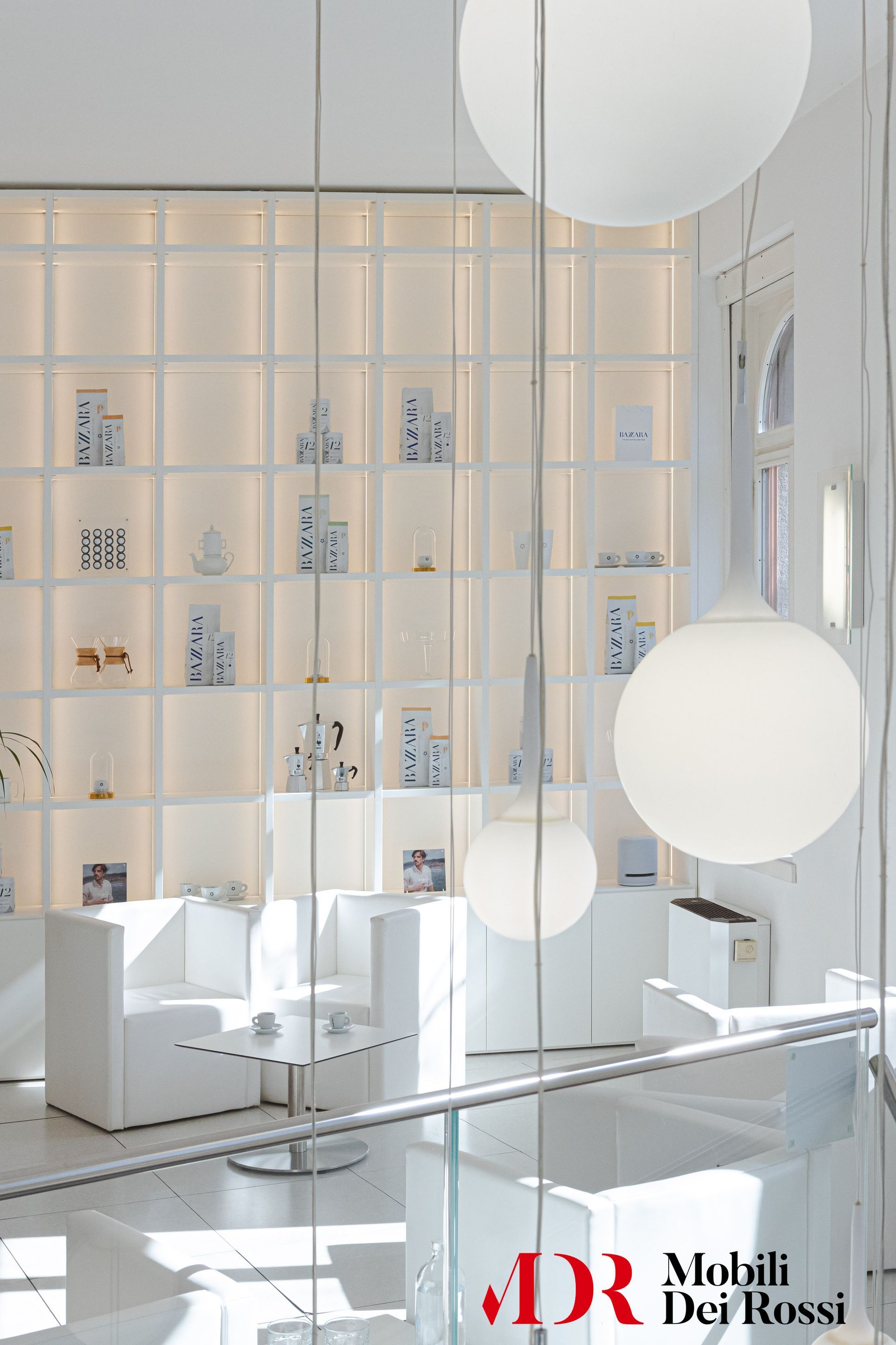 Luminoso soggiorno moderno di colore bianco con scaffali a muro, sedute e lampade a sospensione a forma di globo.