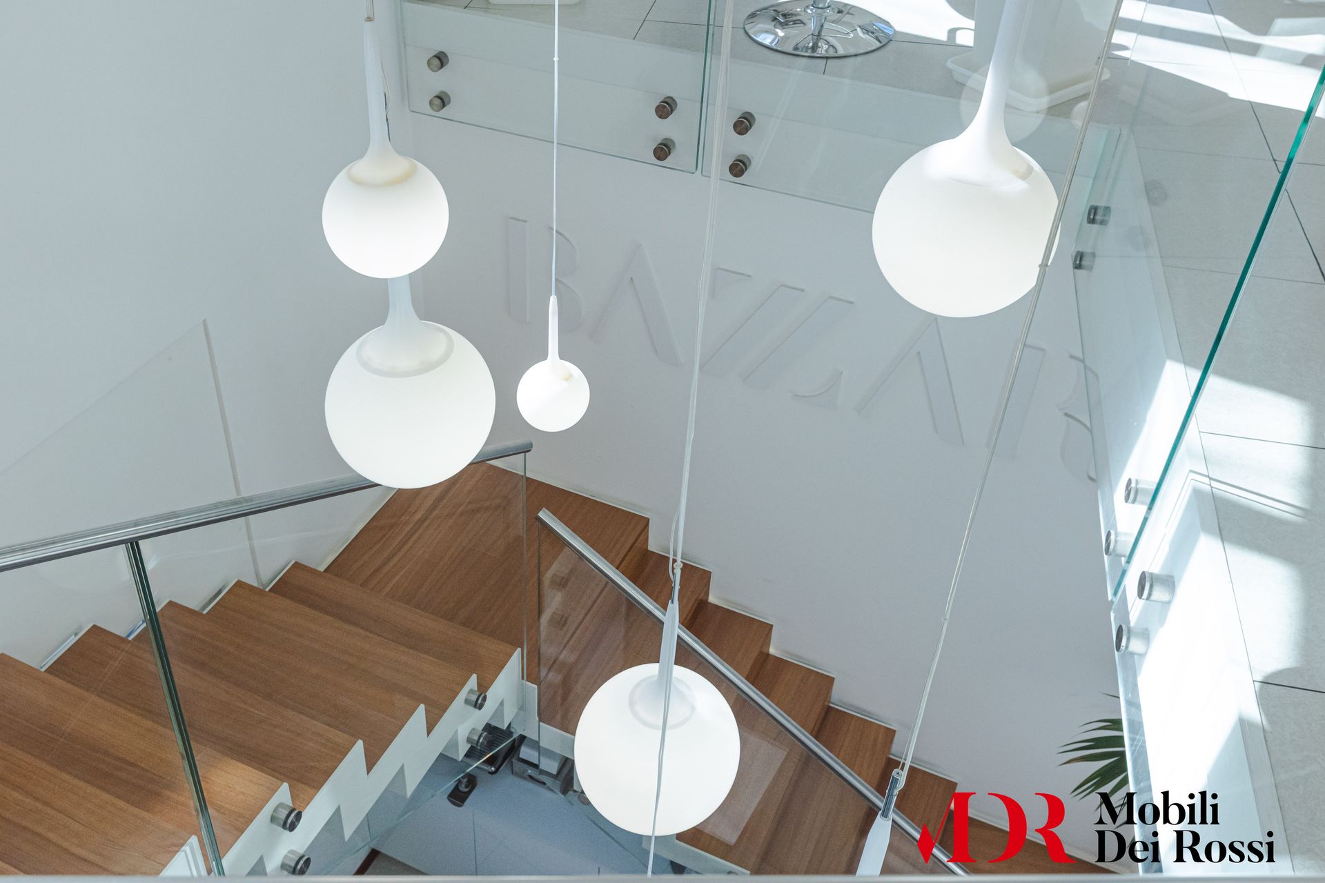 Vista dall'alto di una scala in legno con lampade a sospensione bianche in un luminoso interno moderno.