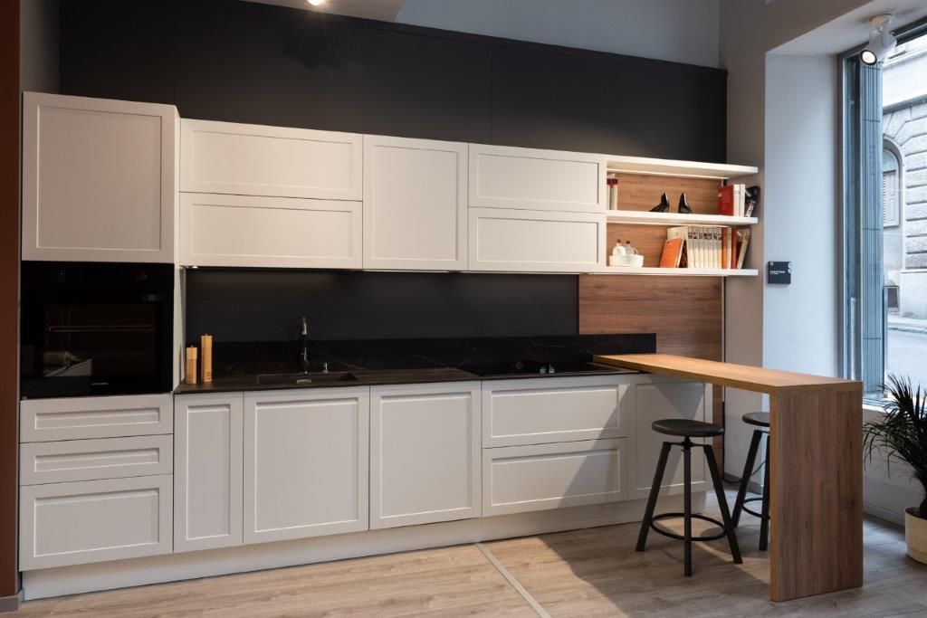 Cucina moderna con mobili bianchi, paraschizzi nero e bancone in legno vicino a una finestra.