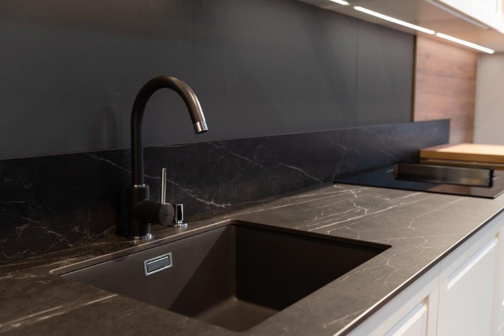 Lavello da cucina moderno con piano di lavoro scuro, rubinetto nero e scolapiatti integrato.