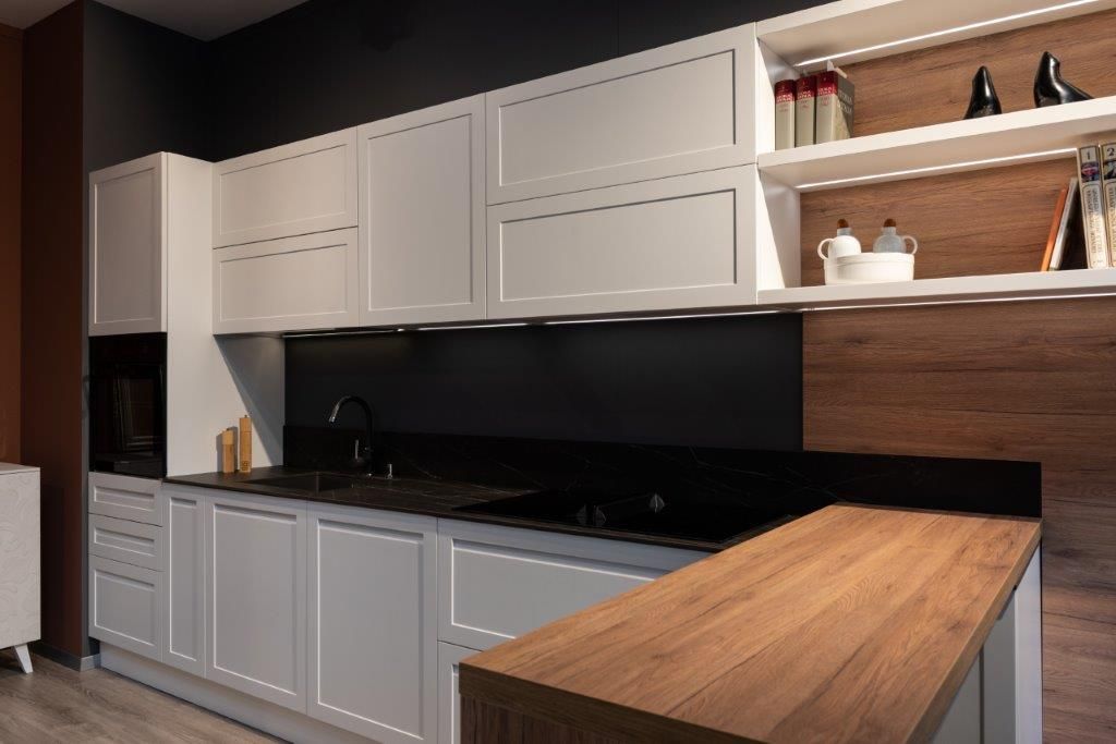 Cucina moderna con mobili bianchi, paraschizzi nero e penisola con piano di lavoro in legno.