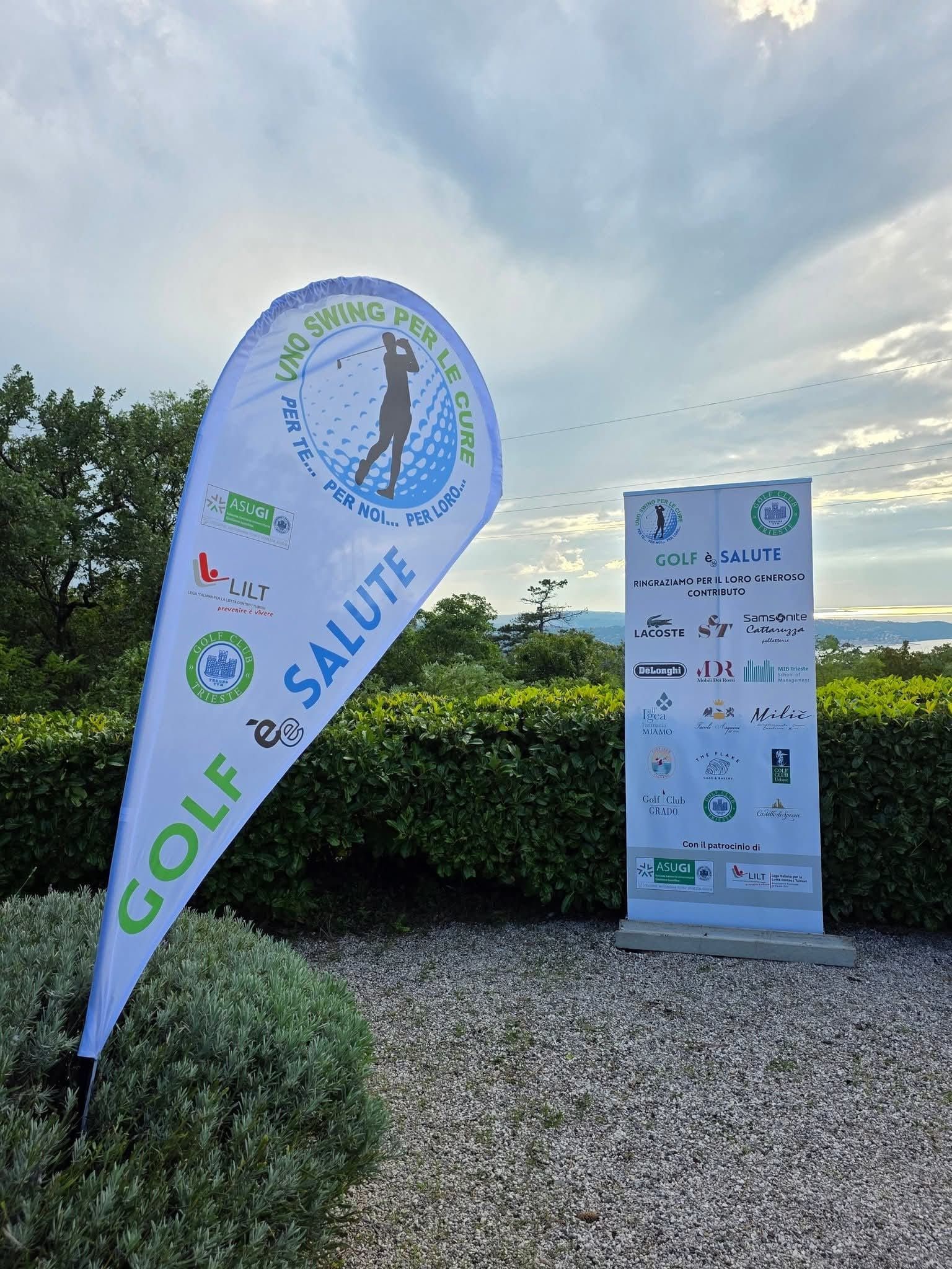 Lo striscione dell'evento Golf et Santé è posizionato accanto al cartello dello sponsor su un sentiero di ghiaia in un soleggiato giardino all'aperto.