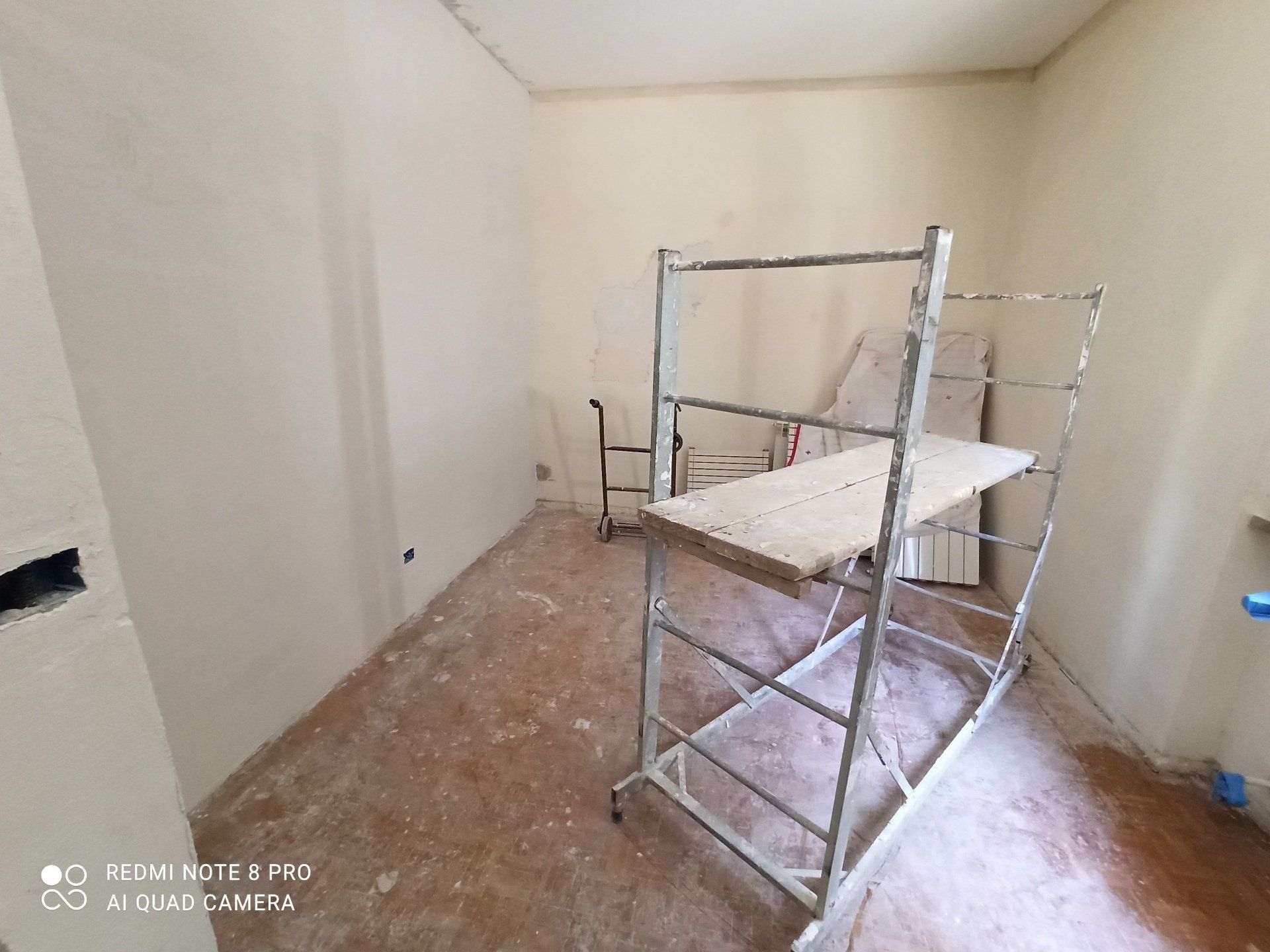 Piccola stanza vuota con pareti bianche e impalcature al centro, in fase di costruzione.