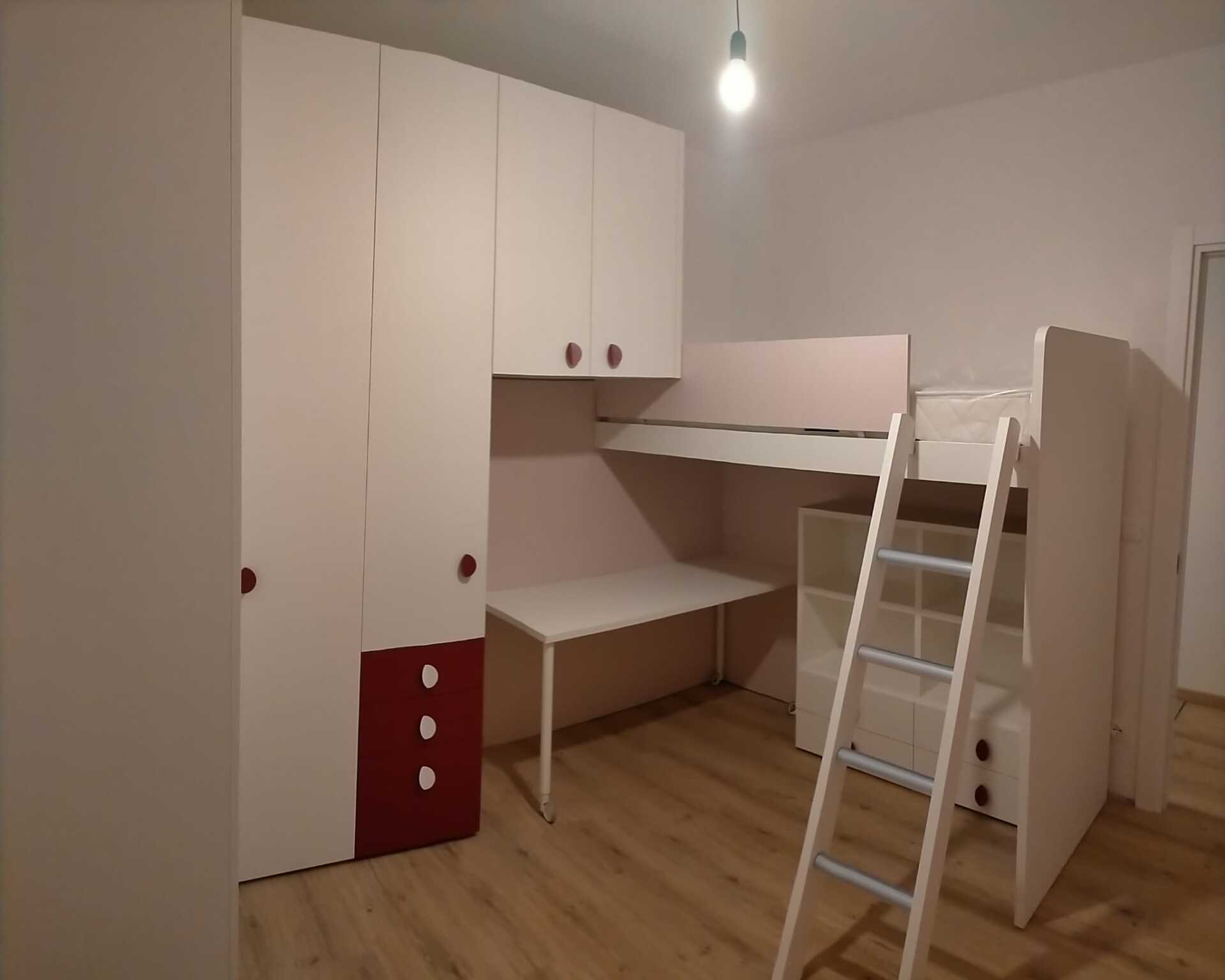 Piccola camera da letto con letto a soppalco bianco, scrivania, armadio e scala su pavimento in legno.