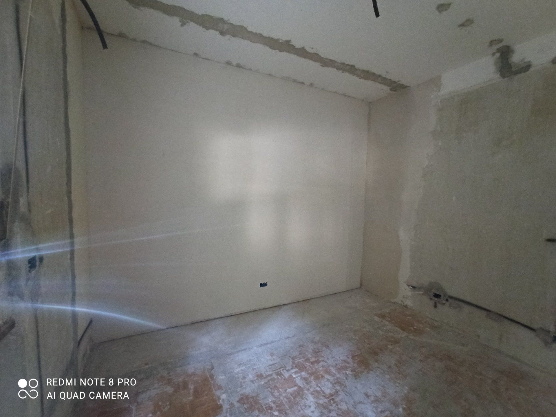 Stanza vuota e non rifinita con pareti spoglie, pavimento in cemento e travi a vista sul soffitto.