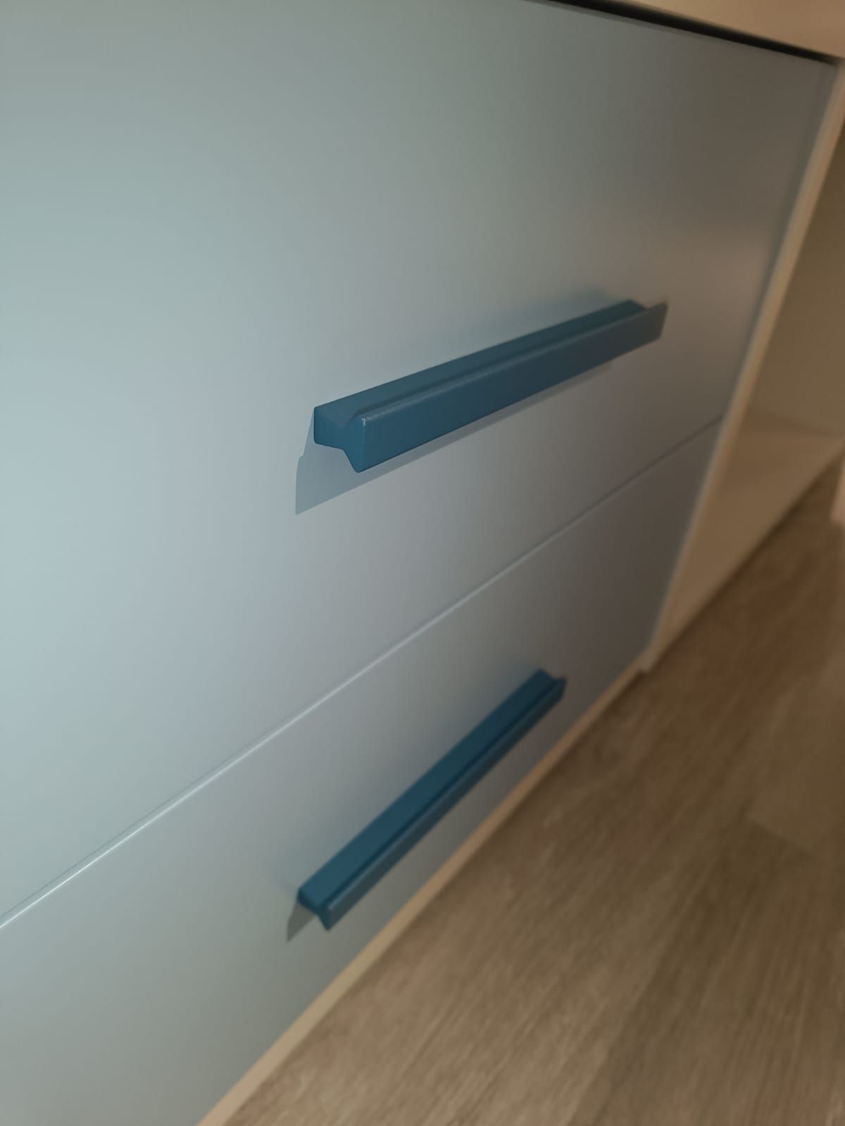 Maniglie blu per cassetti su un mobile bianco accanto a un pavimento in legno.