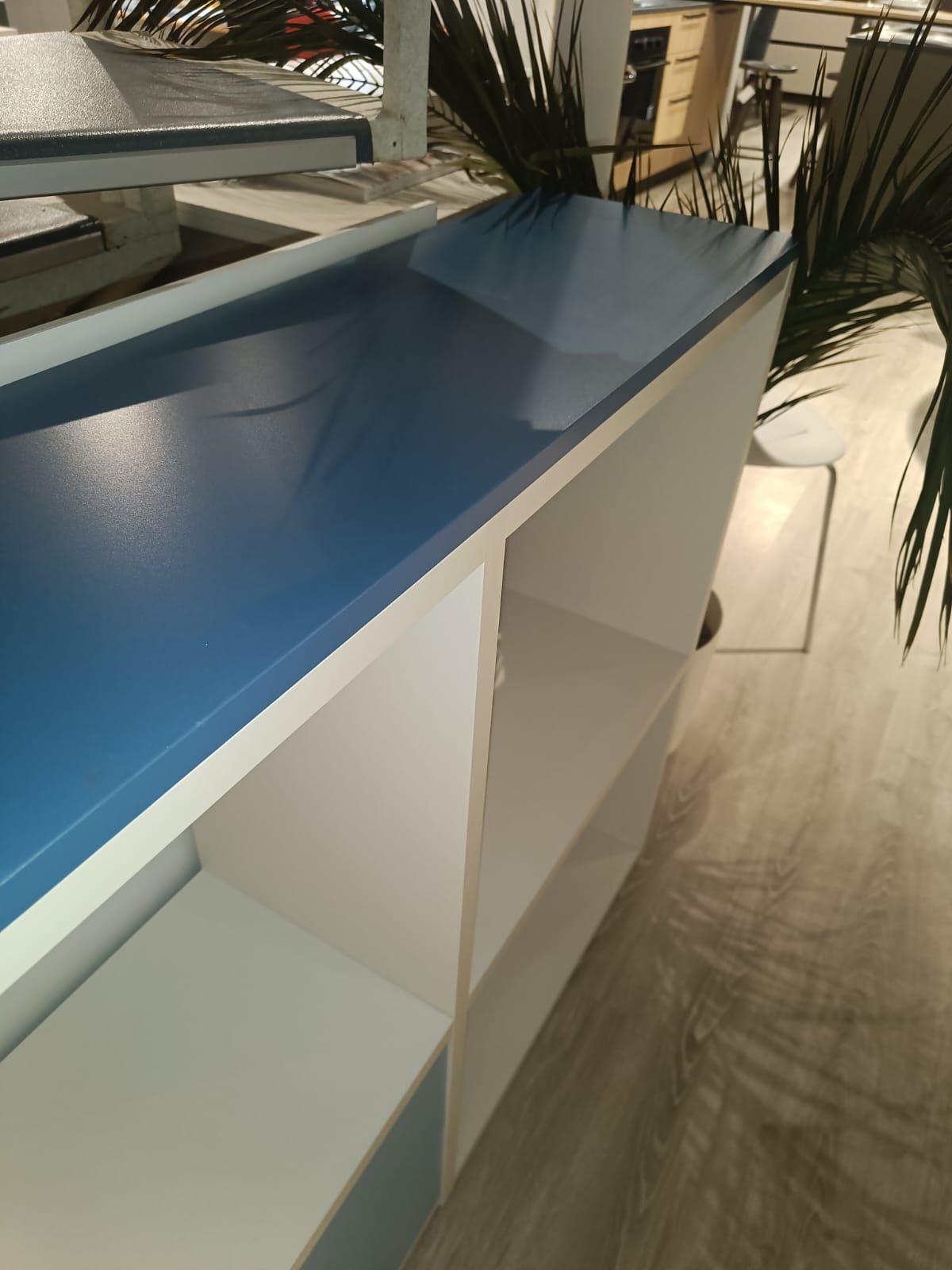Piano di lavoro blu su un mobile bianco in una stanza luminosa con piante da interno e pavimento in legno illuminato dal sole.