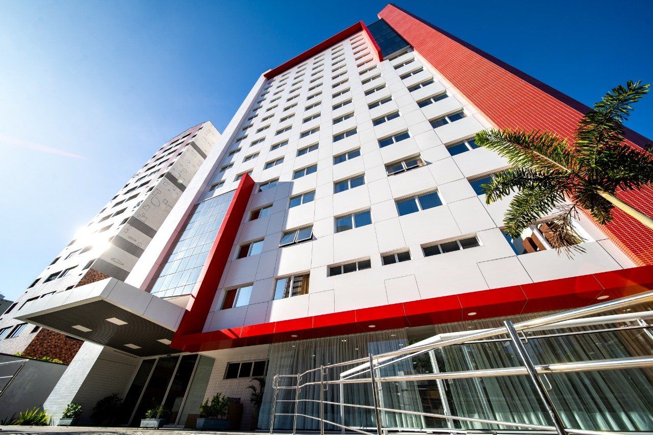Hotel alto com fachada vermelha e branca, sob um céu azul claro.