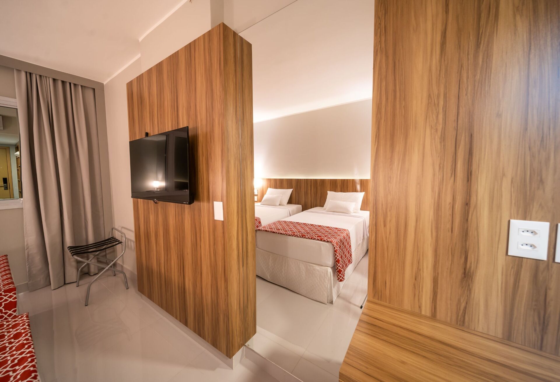 Quarto de hotel com painéis de madeira, TV e duas camas.
