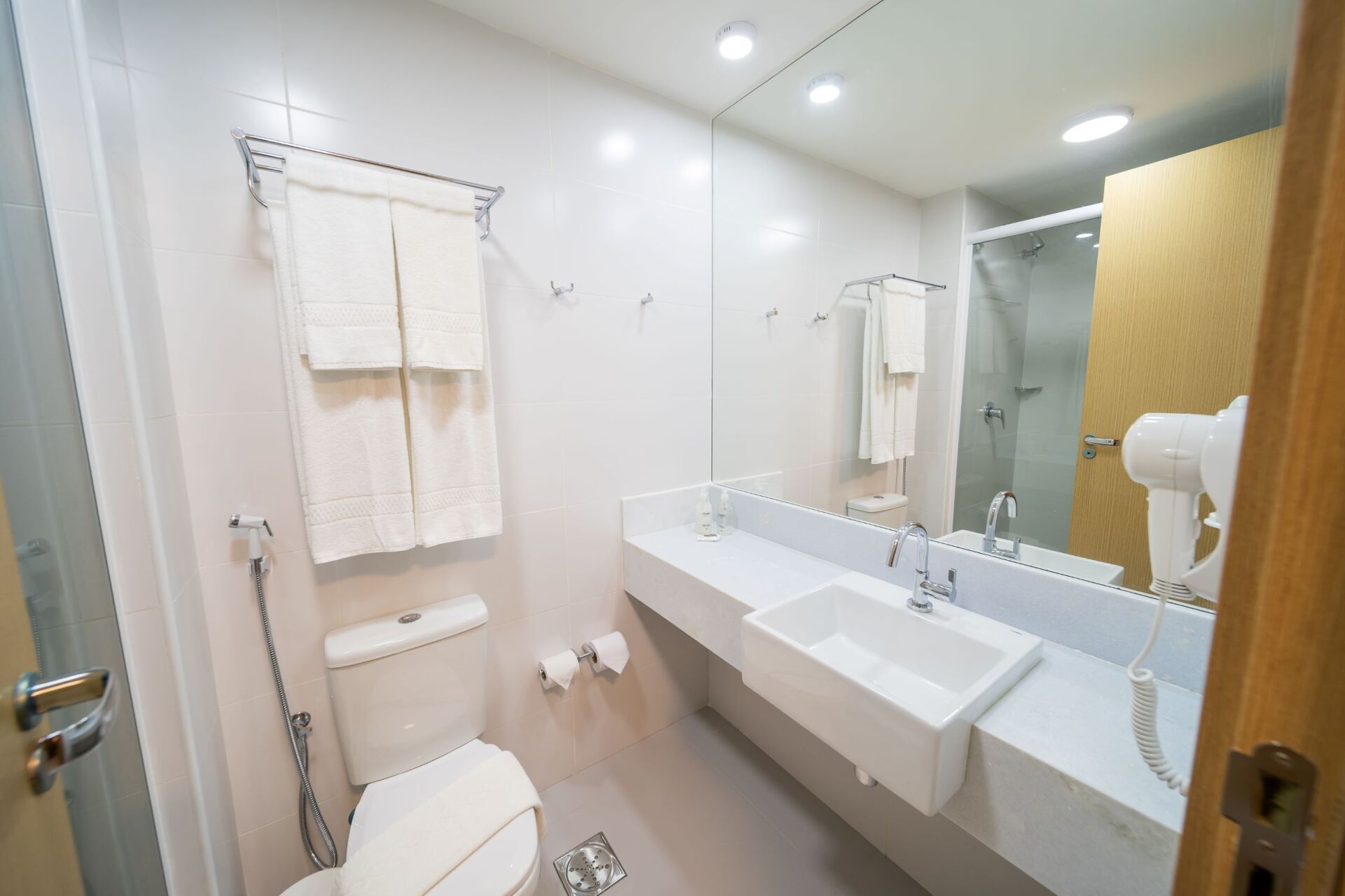 Banheiro moderno com pia branca, vaso sanitário, toalhas e espelho.