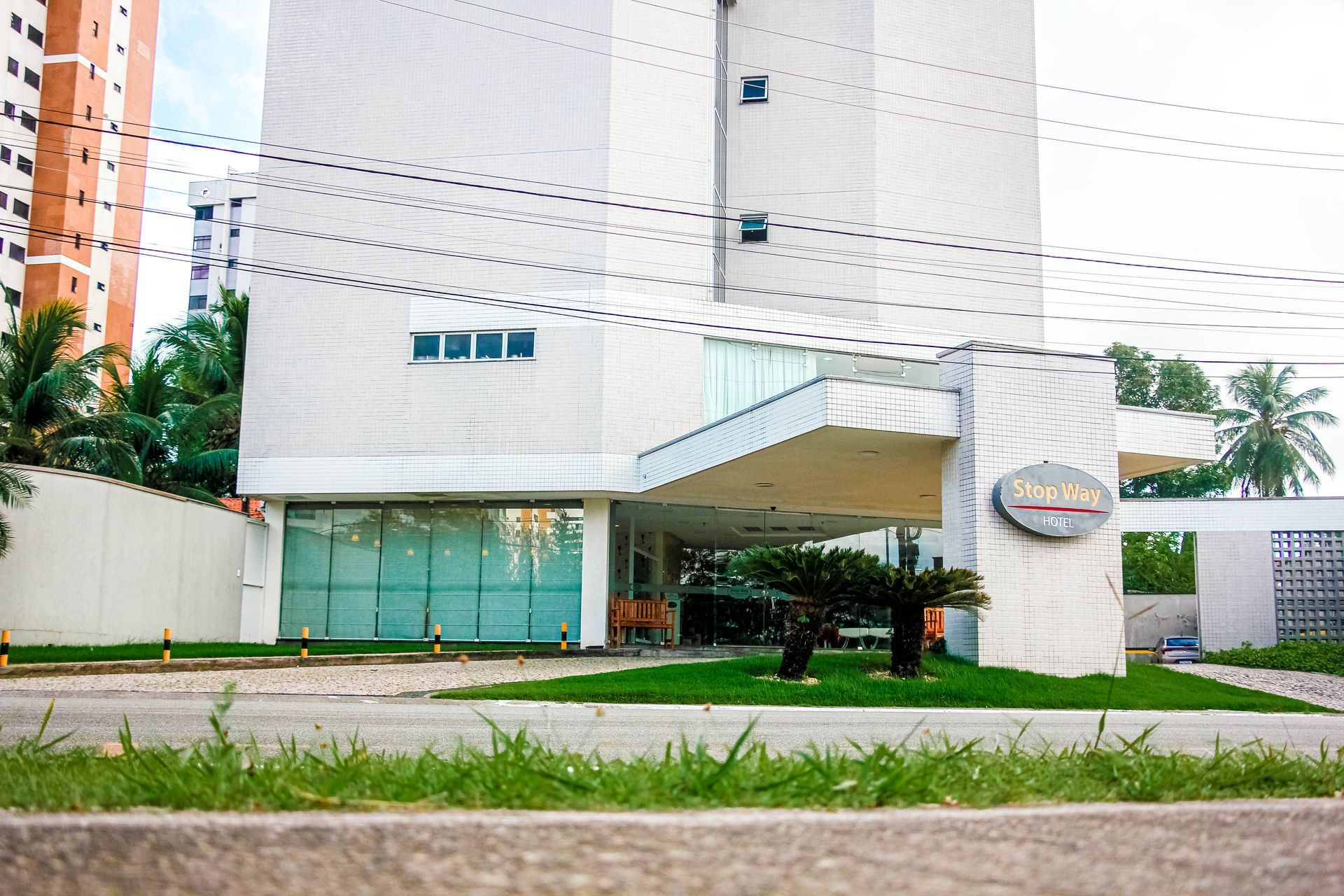 Edifício moderno branco com entrada de vidro, gramado e rua.