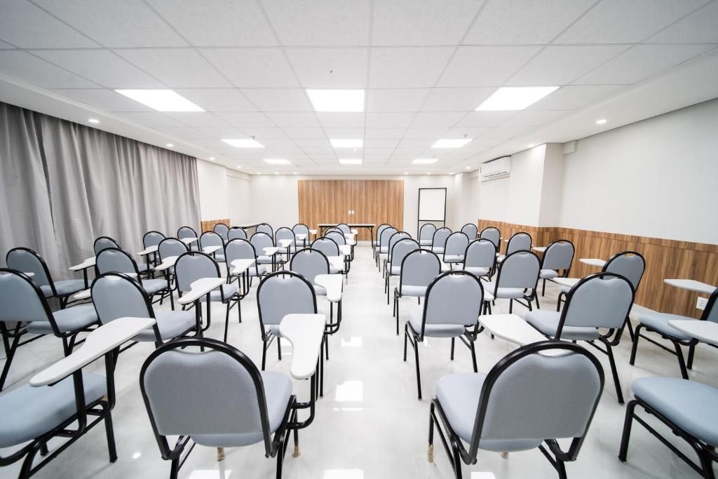 Sala de aula vazia com fileiras de cadeiras e superfícies de escrita anexadas.