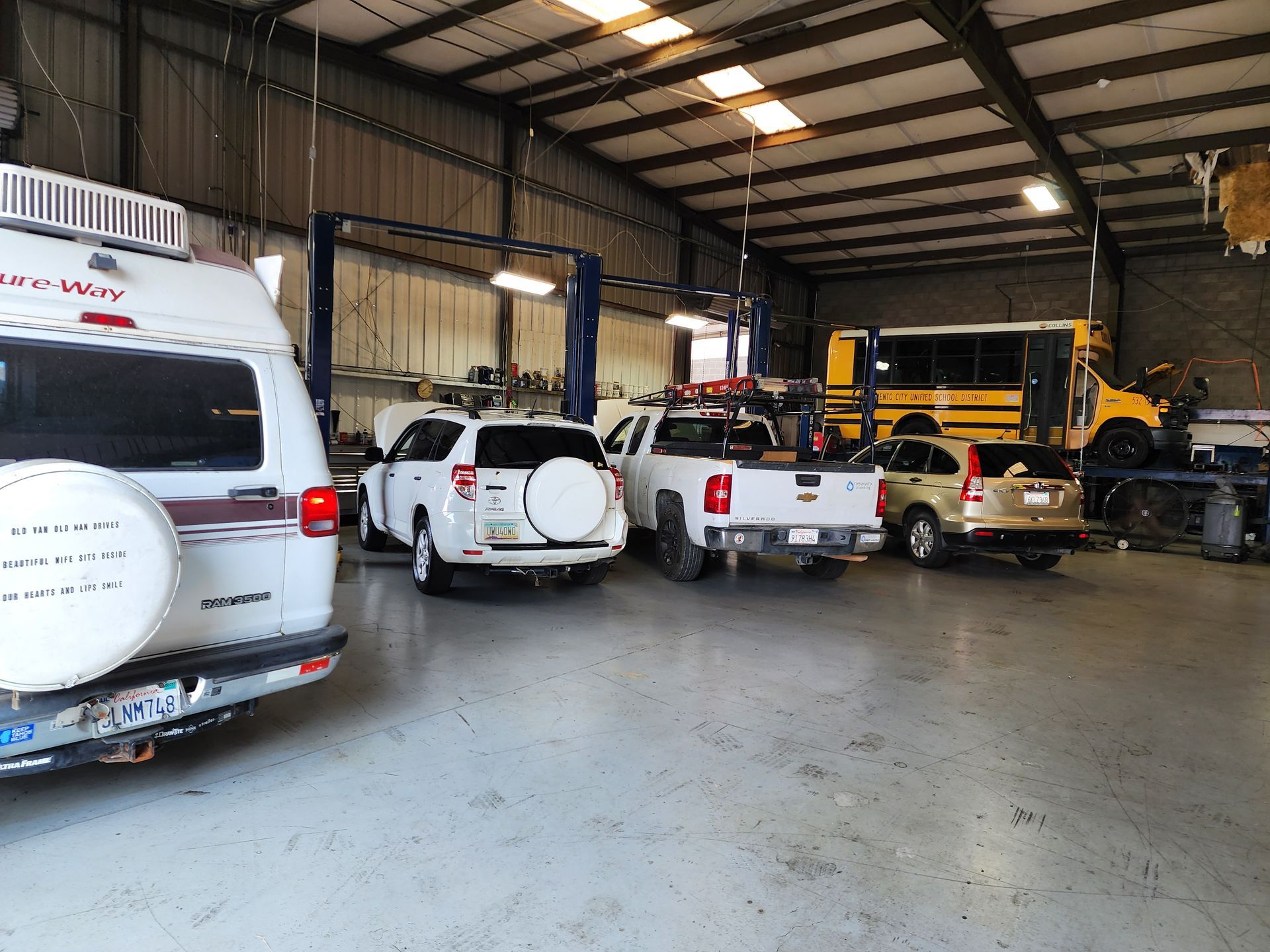 Parking garage with several vehicles, including a white van, SUV, and trucks, under a metal roof | Polar Bear Auto Care