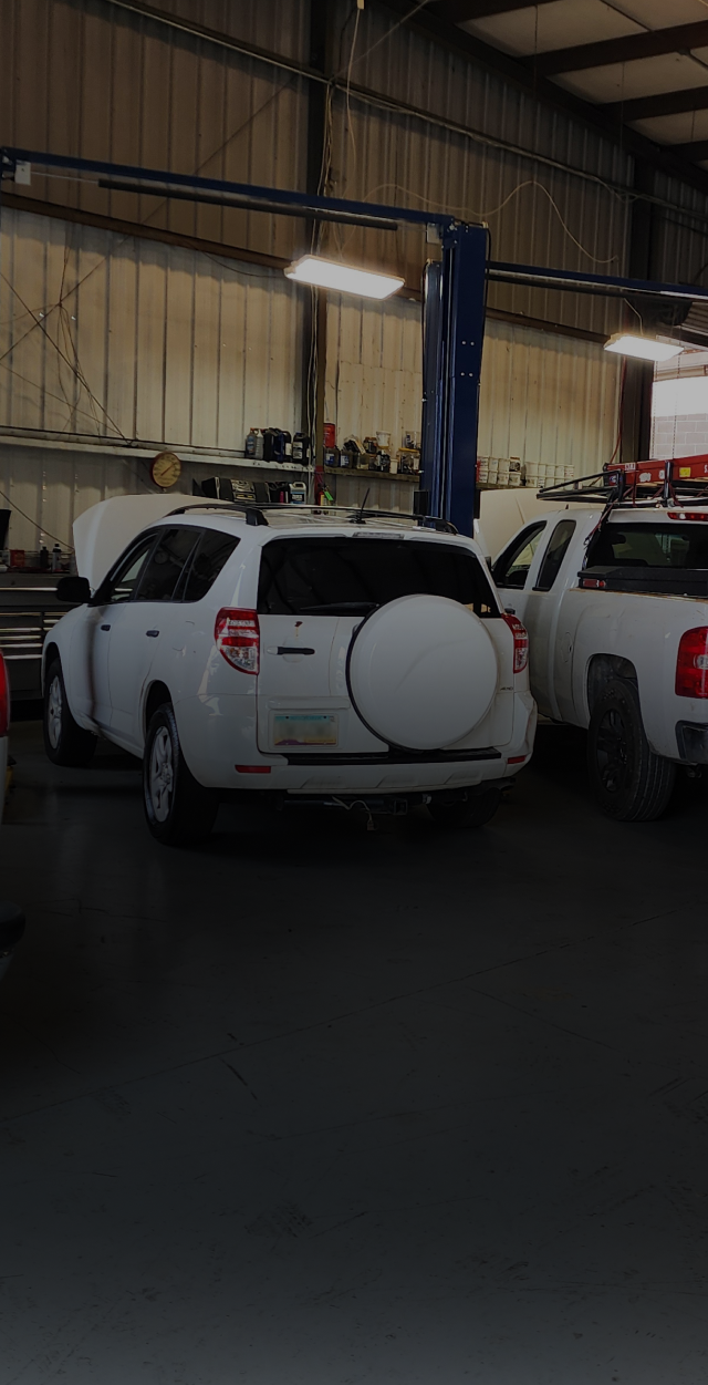 Two white SUVs parked inside an auto repair garage with a blue vehicle lift overhead | Polar Bear Auto Care