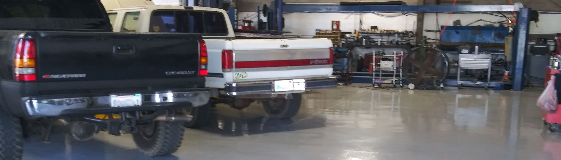 Two pickup trucks parked inside an auto repair garage, with tools and equipment in the background. | Polar Bear Auto Care