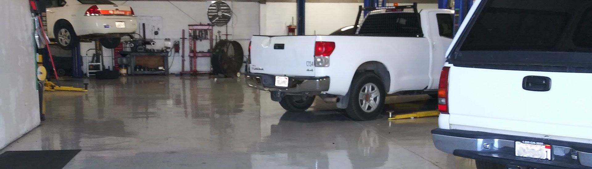Two white pickup trucks parked inside a garage with a glossy wet floor. | Polar Bear Auto Care