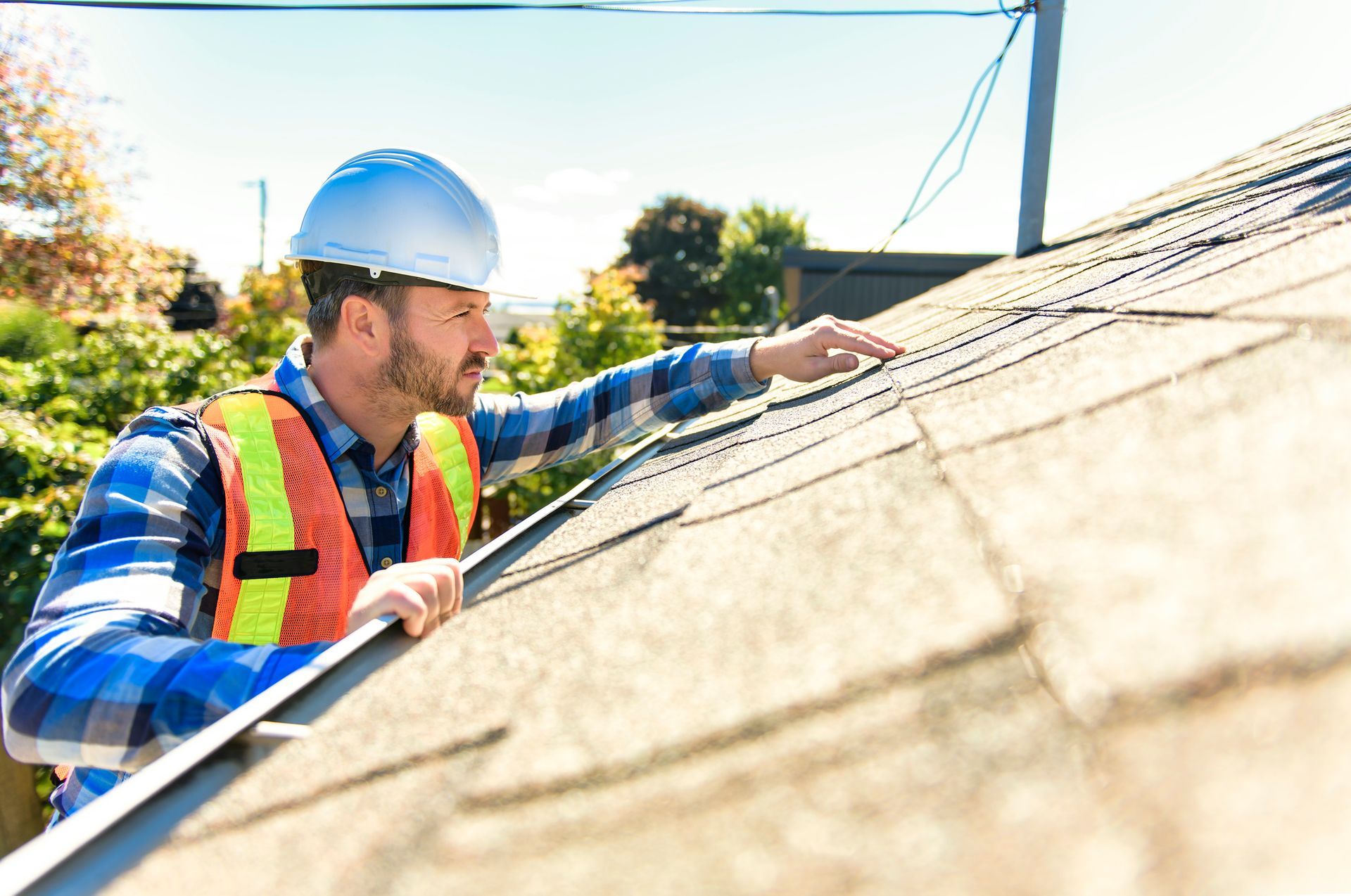 A roofer wearing a white helmet is inspecting a roof, showcasing roofing services.