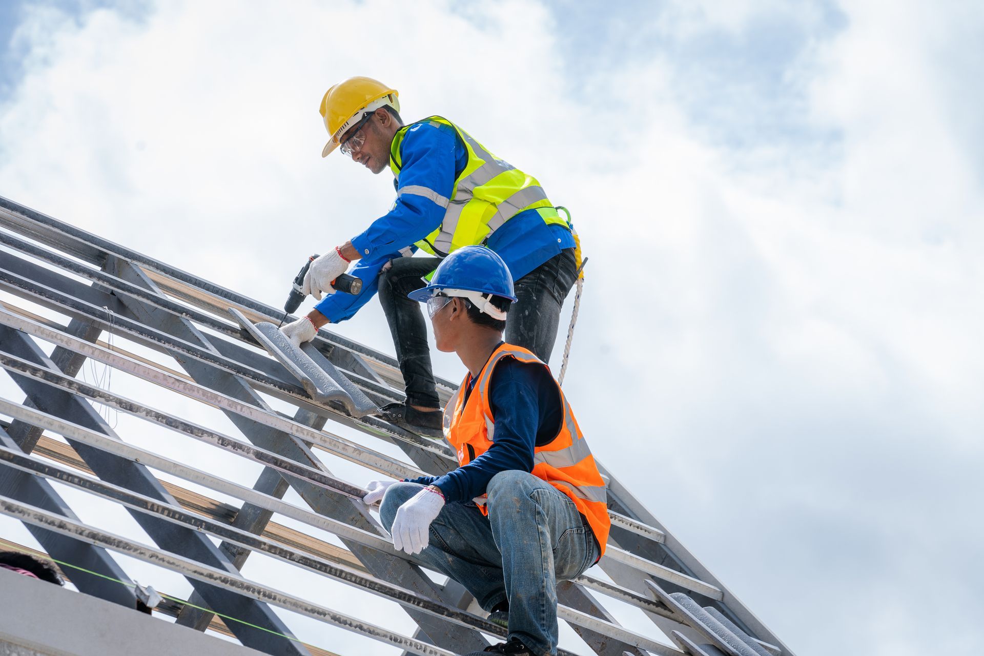 Two workers, in protective gear, performing roof installation on a house, with stacks of roof tiles.