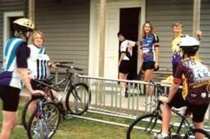 Cyclists in colorful gear standing outside a building. Bikes in view.