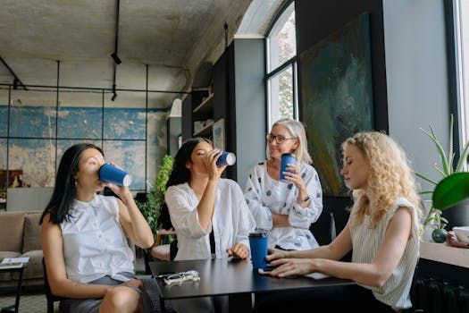 Four friends chatting and drinking at a café table by large windows
