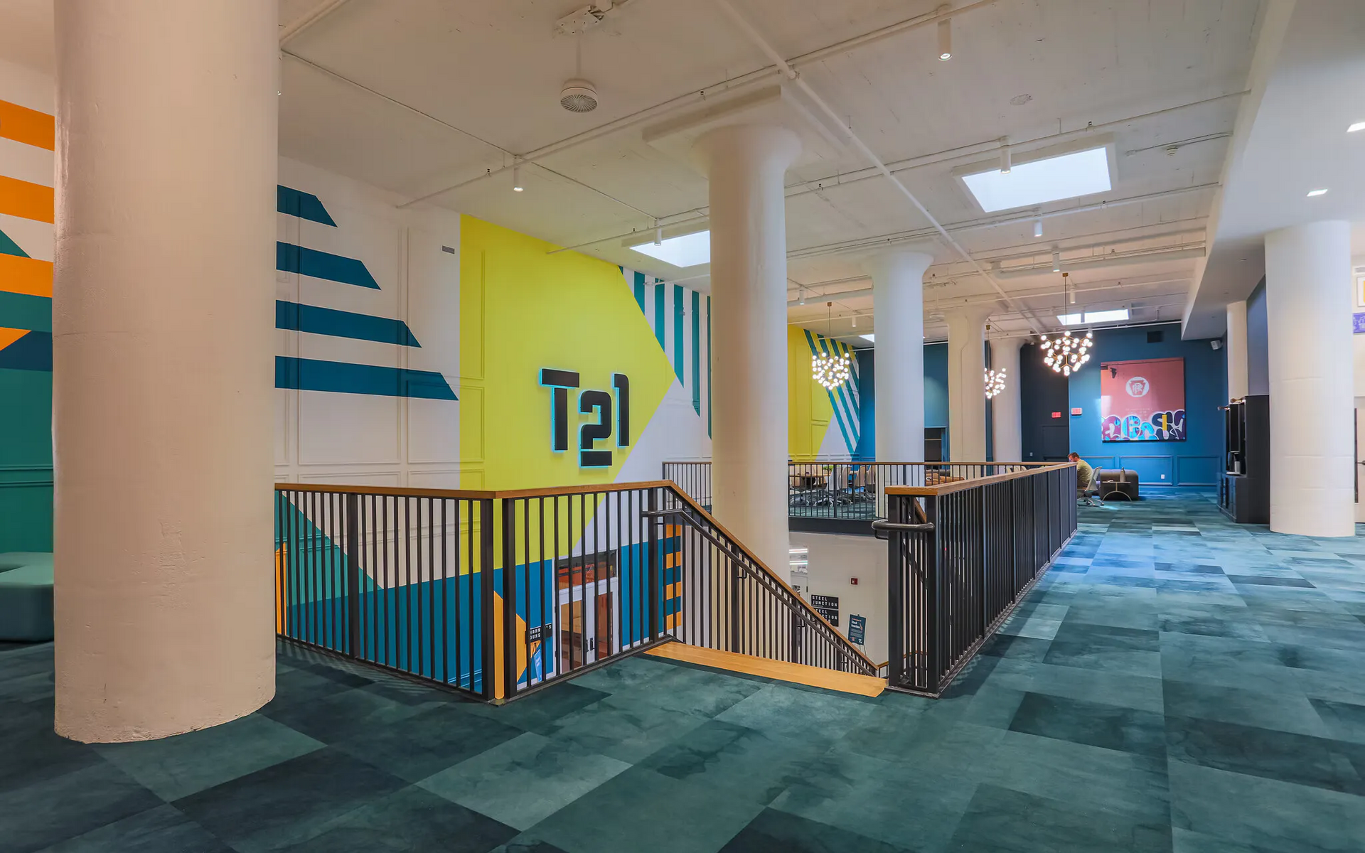 Interior lobby with colorful mural walls, railing, and seating; a person seated in the background at Terminal 21, a premier apartment community in Downtown Pittsburgh, Pennsylvania.