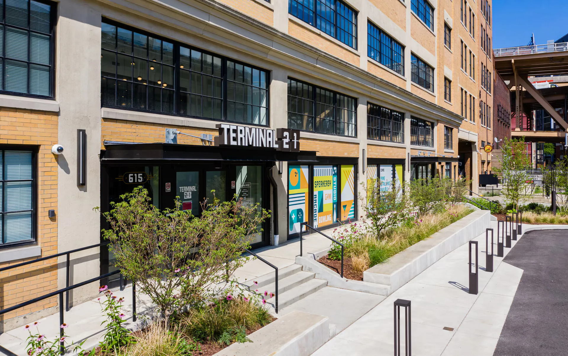 Exterior view of a brick apartment building with a storefront labeled Terminal 21 and a landscaped walkway at Terminal 21, a premier apartment community in Downtown Pittsburgh, Pennsylvania.