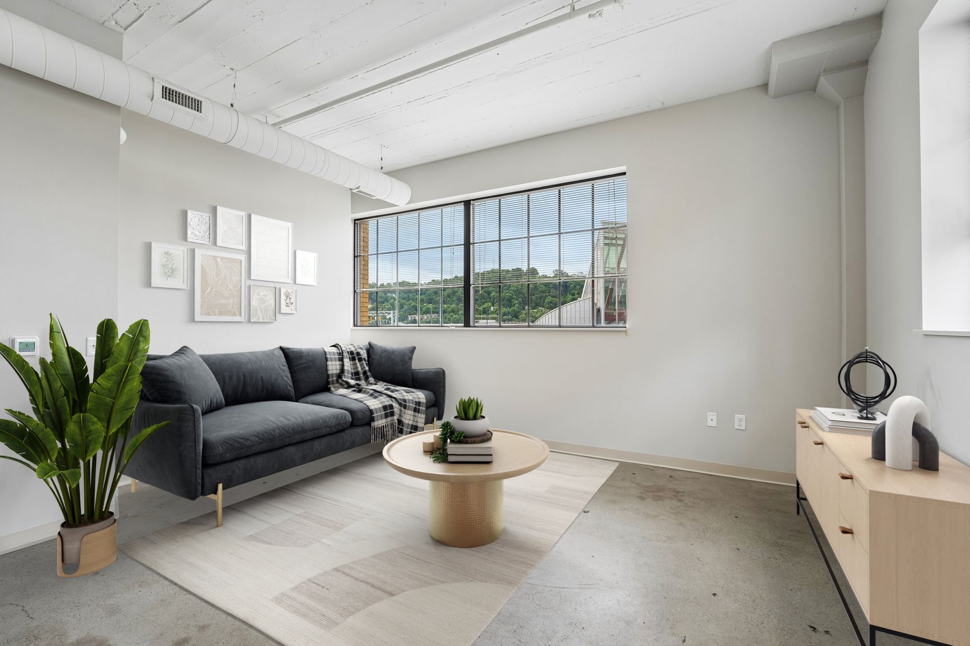 Bright living room with gray sofa, round coffee table, large window, potted plant, and TV console at Terminal 21, a premier apartment community in Downtown Pittsburgh, Pennsylvania.