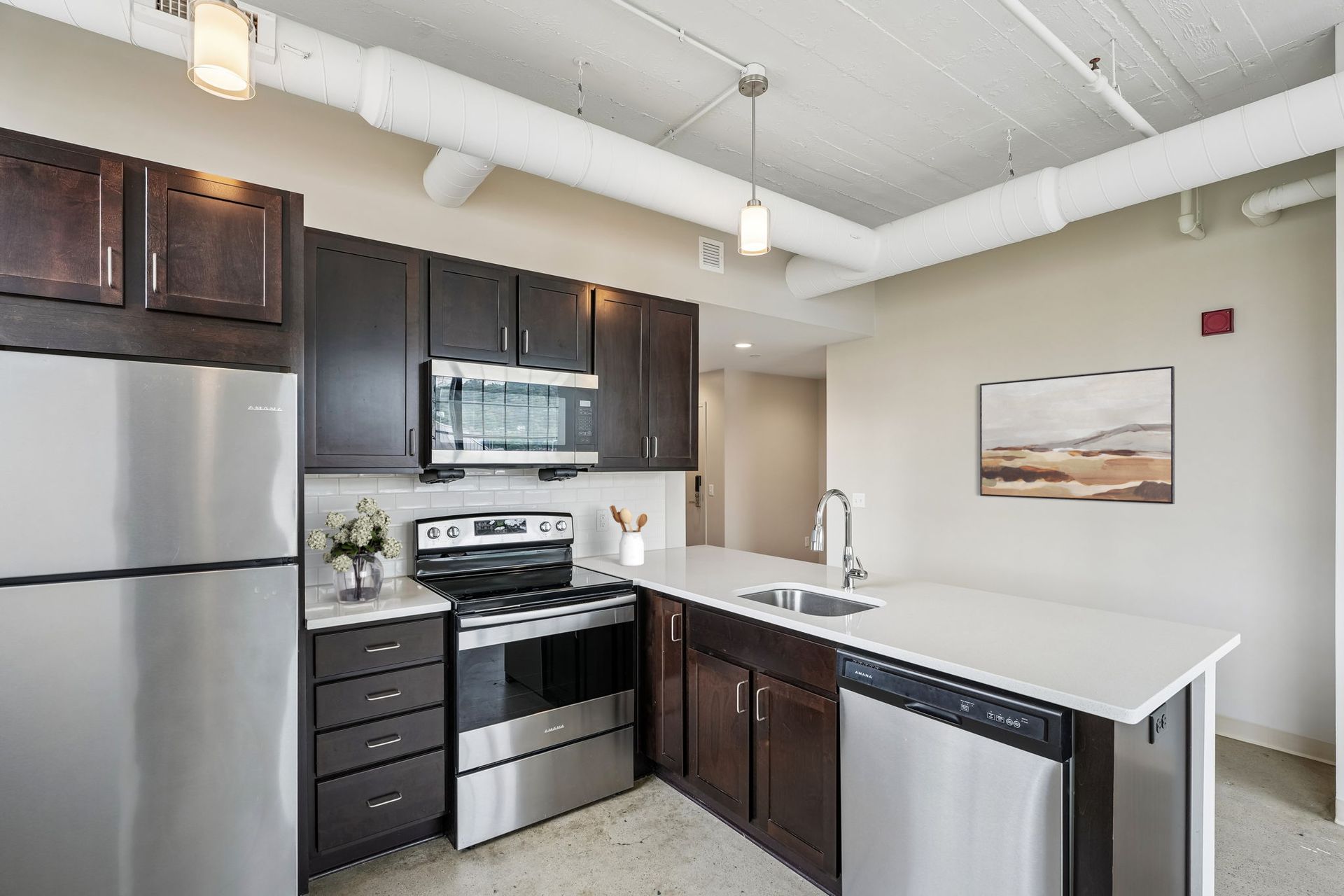 Modern kitchen with stainless steel appliances, dark cabinets, white countertops, and breakfast bar at Terminal 21, a premier apartment community in Downtown Pittsburgh, Pennsylvania.