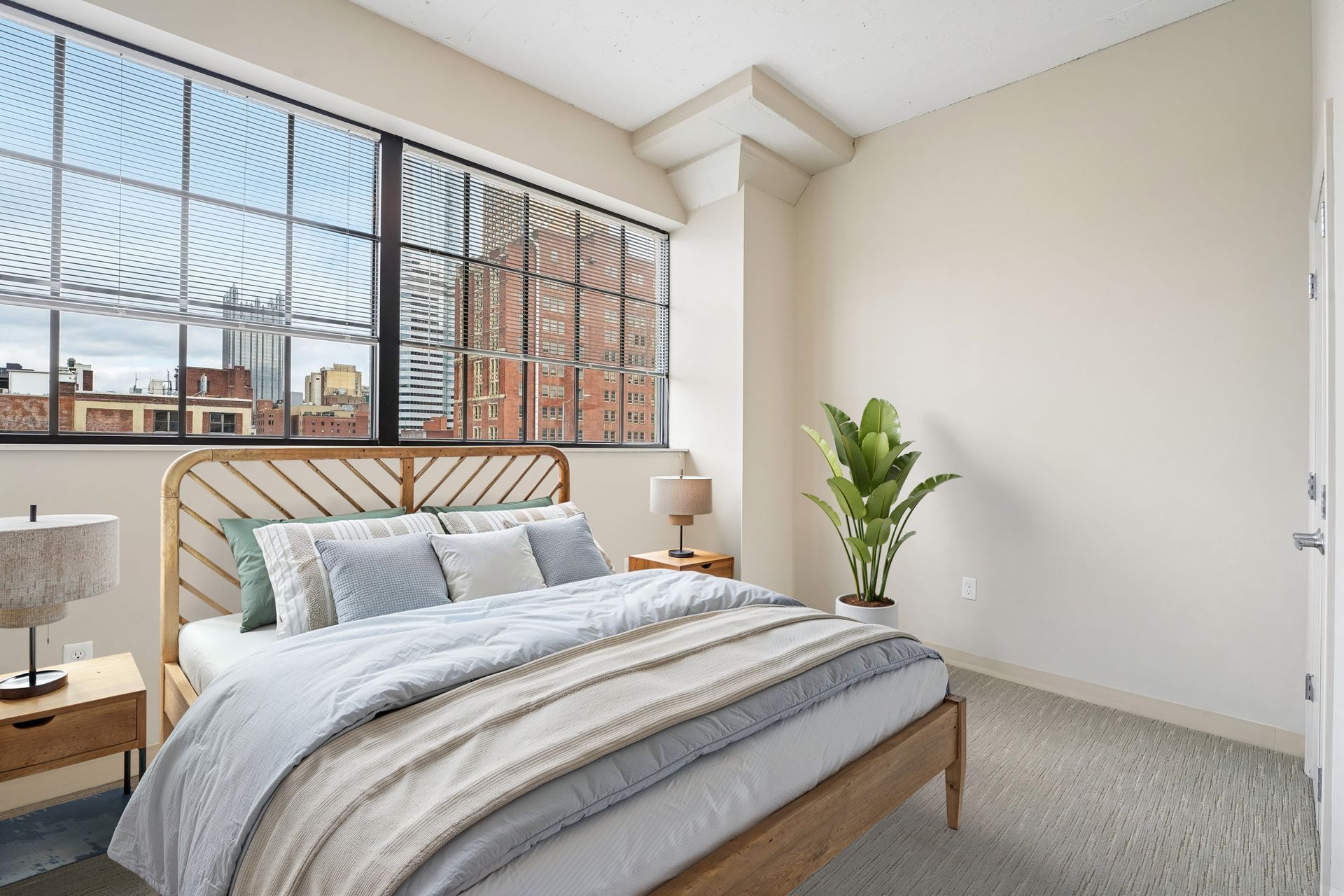 Bright bedroom with a bed, large window, and potted plant in a modern apartment at Terminal 21, a premier apartment community in Downtown Pittsburgh, Pennsylvania.