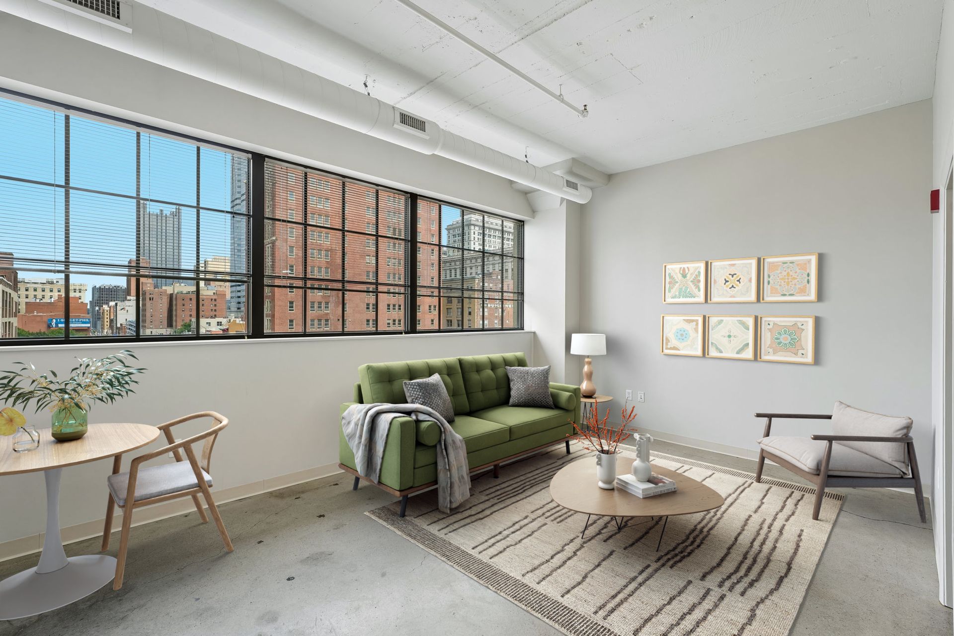 Bright living room with green sofa, large windows, woven rug, and wall art at Terminal 21, a premier apartment community in Downtown Pittsburgh, Pennsylvania.