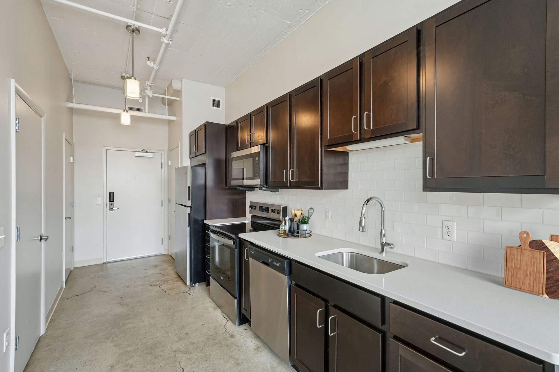 Modern kitchen with dark cabinets, stainless appliances, white countertops, and a hallway entrance at Terminal 21, a premier apartment community in Downtown Pittsburgh, Pennsylvania.