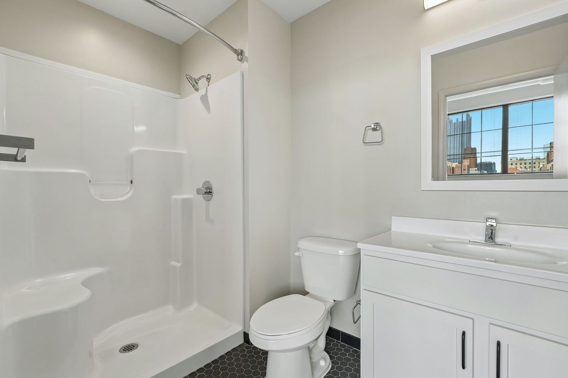 Bright bathroom with white shower, toilet, and vanity beside a window at Terminal 21, a premier apartment community in Downtown Pittsburgh, Pennsylvania.