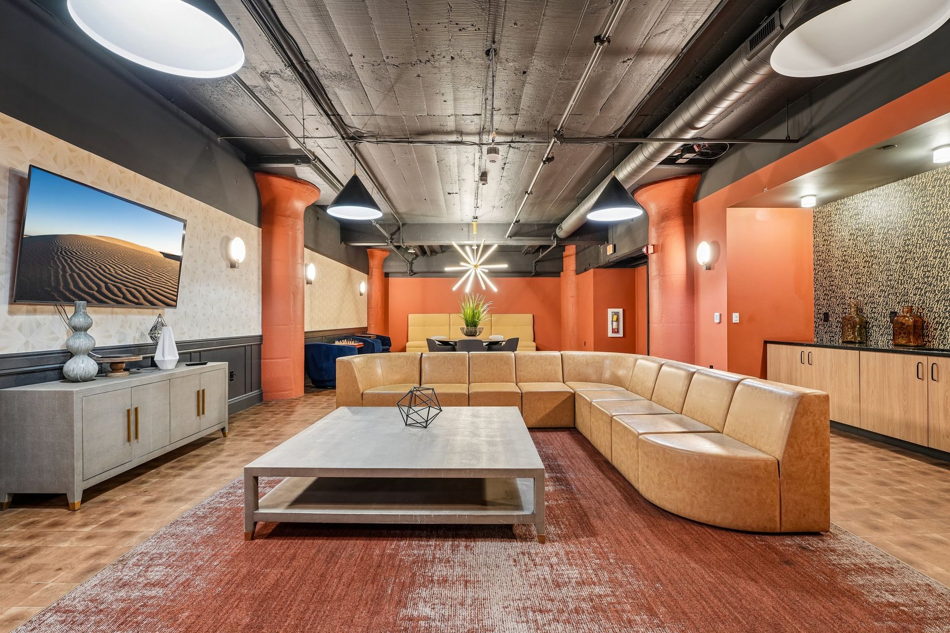 Modern living room with orange walls, beige sectional sofa, coffee table, and abstract wall art at Terminal 21, a premier apartment community in Downtown Pittsburgh, Pennsylvania.