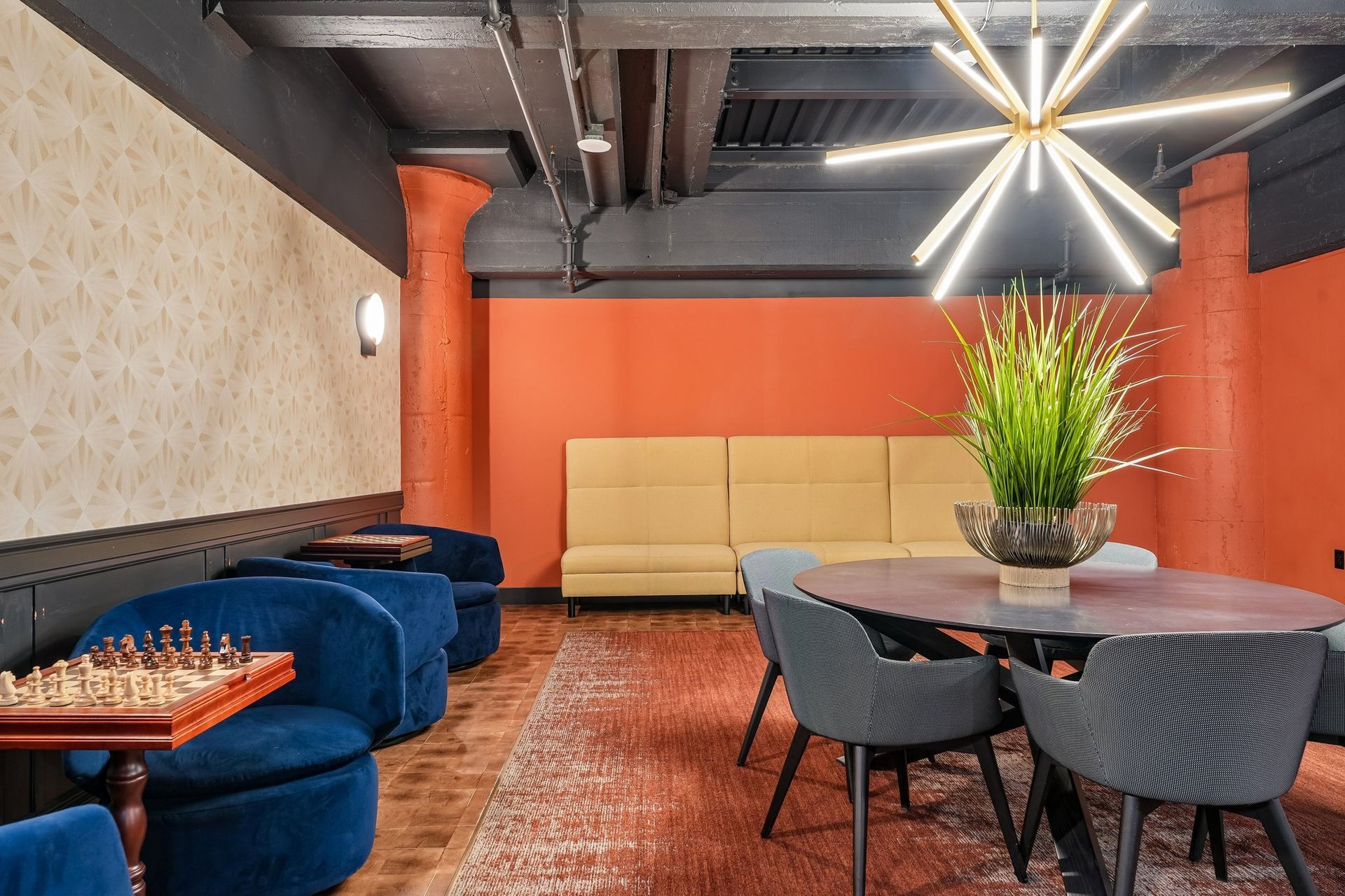 Stylish lounge with blue and beige sofas, round table, red walls, patterned rug, and modern starburst light fixture at Terminal 21, a premier apartment community in Downtown Pittsburgh, Pennsylvania.
