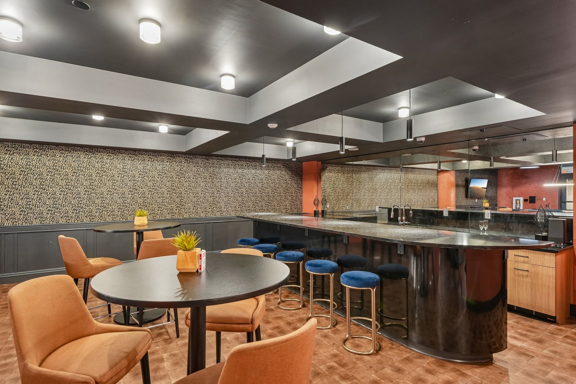 Modern bar and lounge with round tables, orange chairs, blue stools, and a mirrored counter under ceiling lights at Terminal 21, a premier apartment community in Downtown Pittsburgh, Pennsylvania.