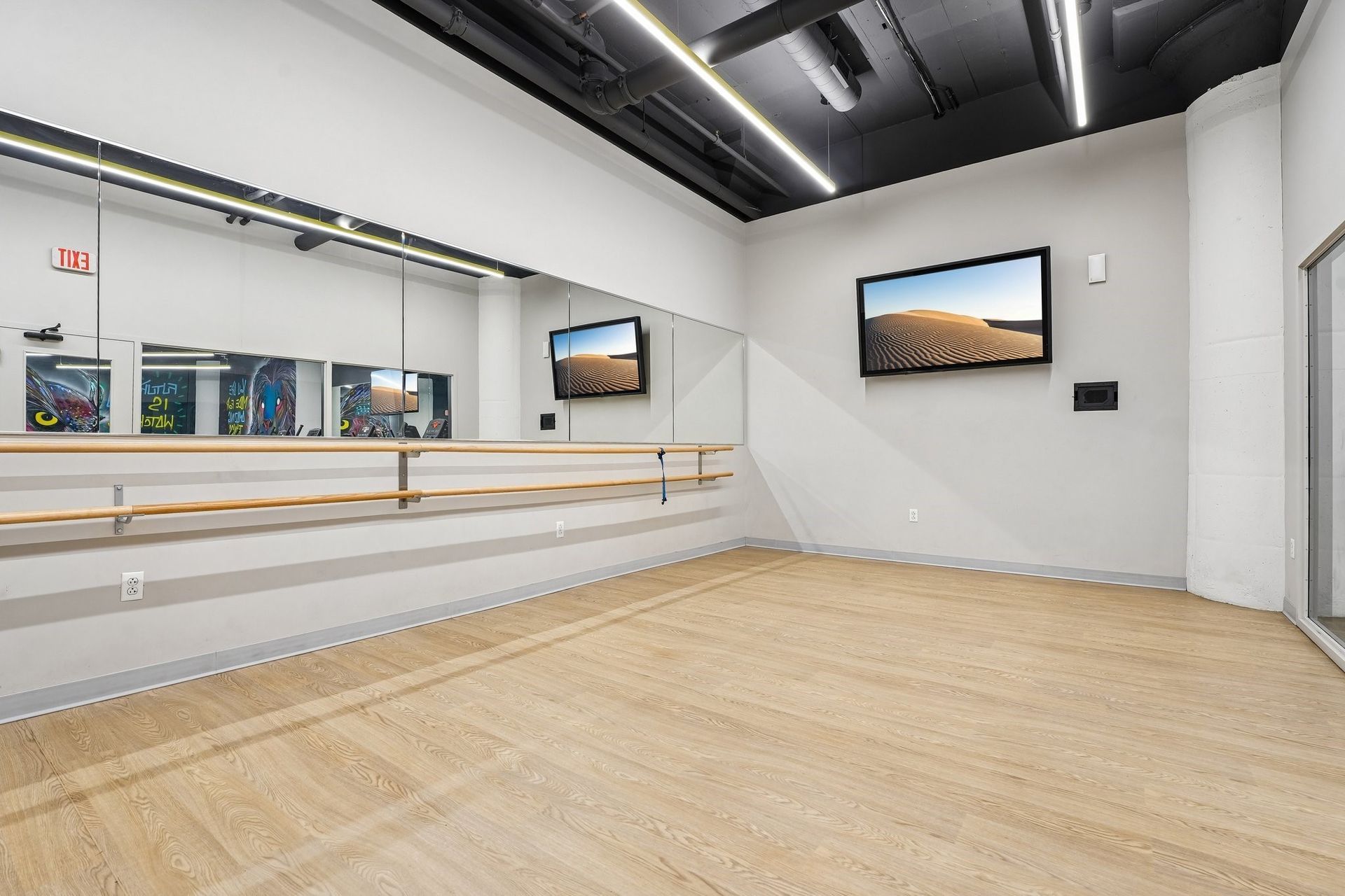 Empty modern yoga studio with hardwood floor, ballet barre, mirrors, and TV at Terminal 21, a premier apartment community in Downtown Pittsburgh, Pennsylvania.