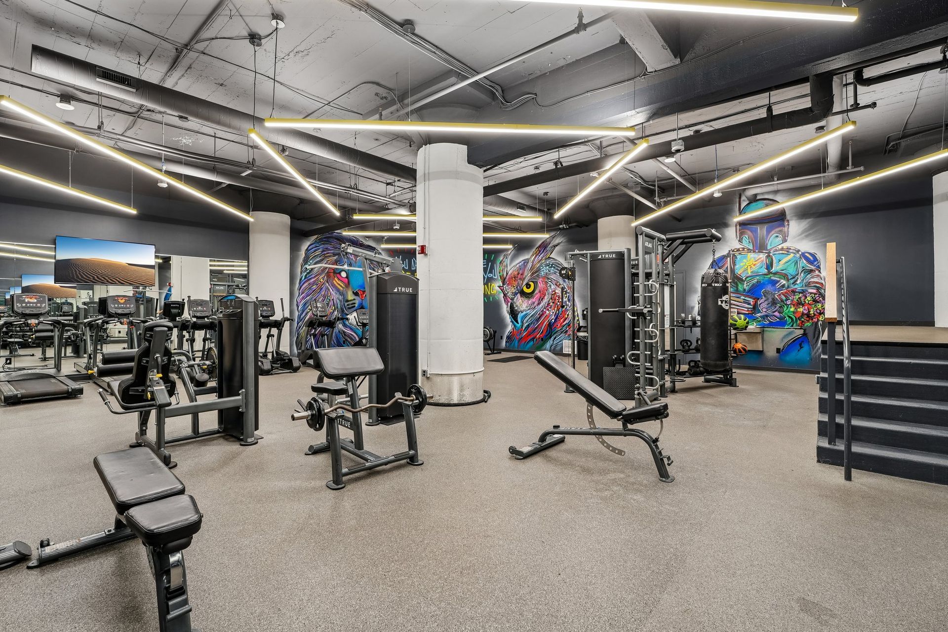 Modern gym with weight machines, benches, and colorful mural walls under bright industrial lighting at Terminal 21, a premier apartment community in Downtown Pittsburgh, Pennsylvania.