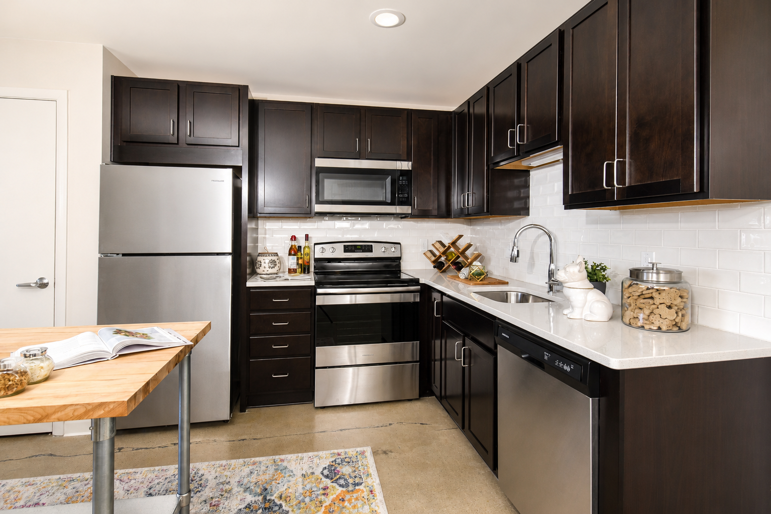 Modern kitchen with dark cabinets, stainless steel appliances, and a wooden table beside a white countertop at Terminal 21, a premier apartment community in Downtown Pittsburgh, Pennsylvania.