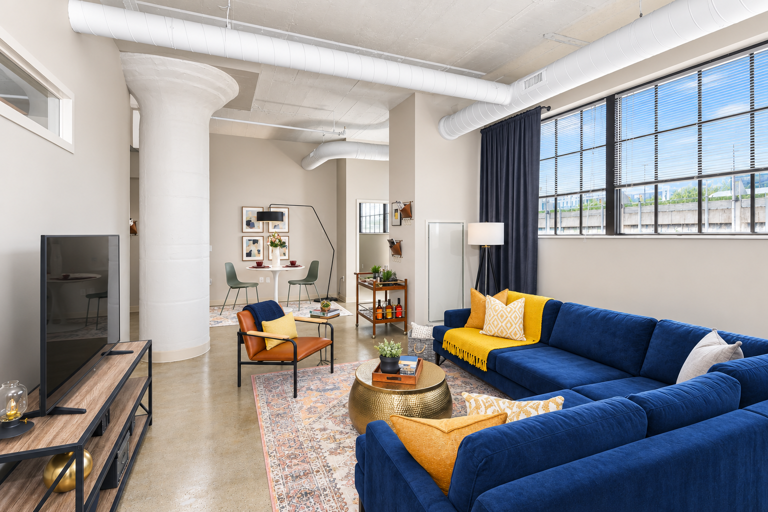 Bright living room with a blue sectional sofa, yellow pillows, orange chair, and tall white columns at Terminal 21, a premier apartment community in Downtown Pittsburgh, Pennsylvania.